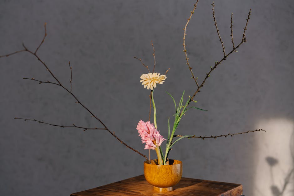 A minimalist floral arrangement in a wooden vase with branches and soft lighting.
