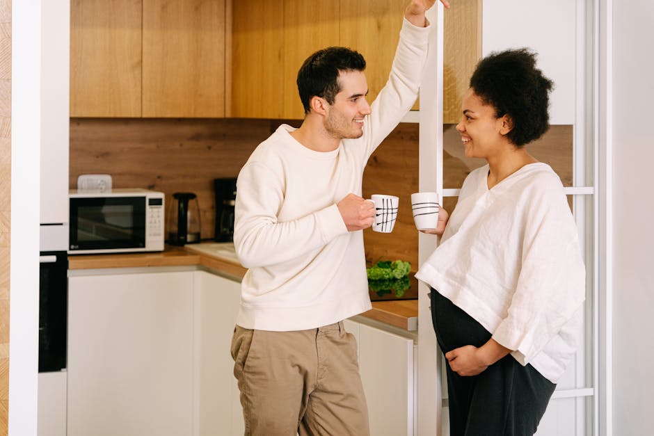 A happy interracial couple shares a coffee break in the kitchen, celebrating pregnancy moments.