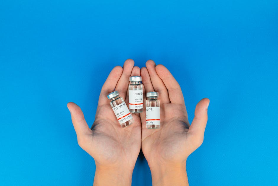 Hands holding COVID-19 vaccine vials against a blue background, symbolizing hope and health.