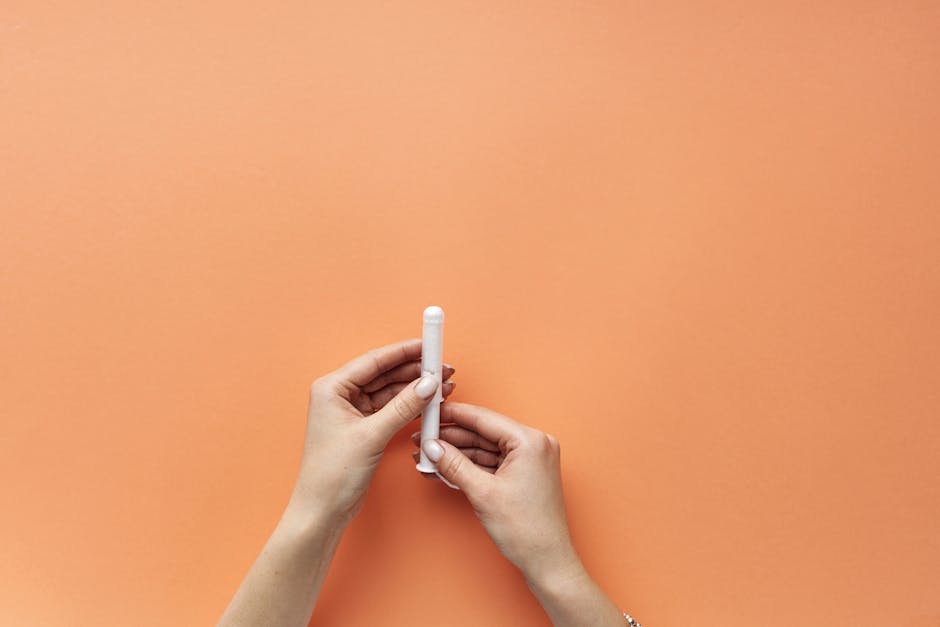 Close-up of female hands holding a tampon on an orange background, symbolizing menstrual hygiene.