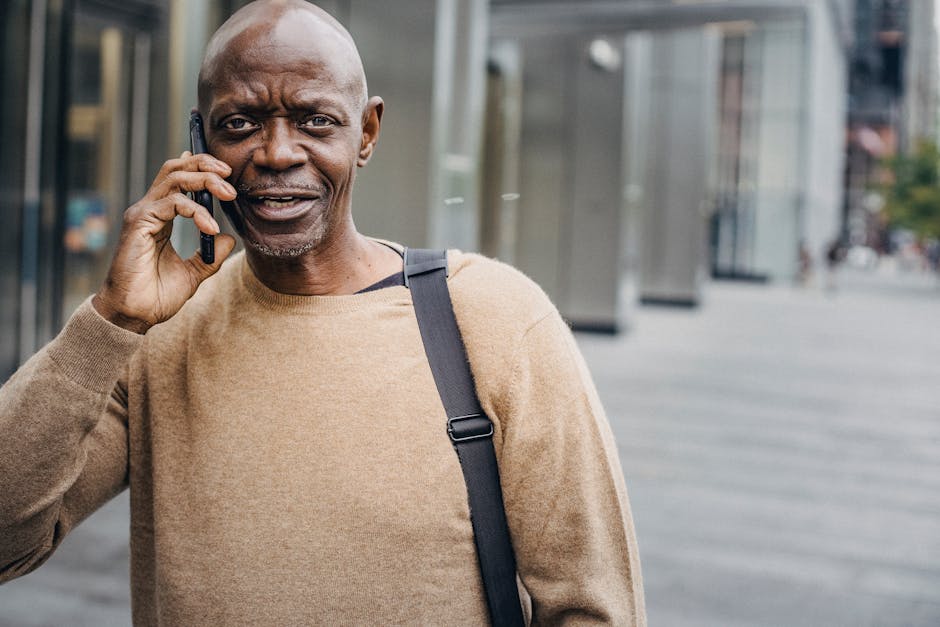 Middle-aged black man in urban setting having a phone conversation outdoors in a casual outfit.