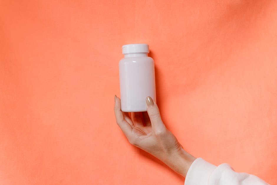 A close-up of a hand holding a white bottle against a vibrant orange background.