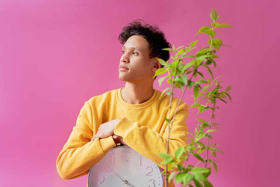 Man holding a clock next to a plant against a pink background, symbolizes time and nature.