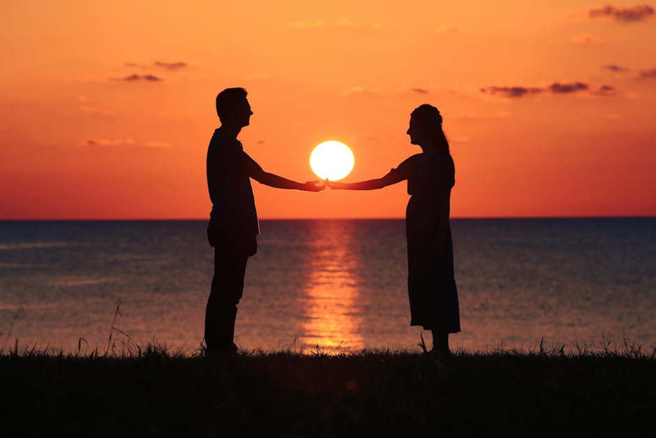 Silhouette of a couple holding the sun at sunset by the sea, symbolizing love and togetherness.