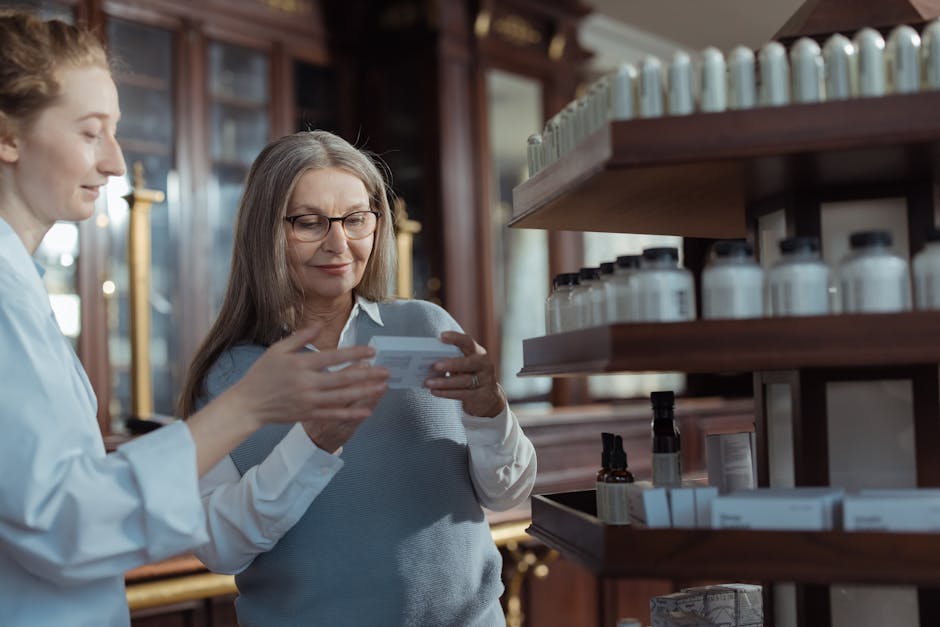 Elderly woman receiving assistance from a pharmacist in a pharmacy with product shelves.