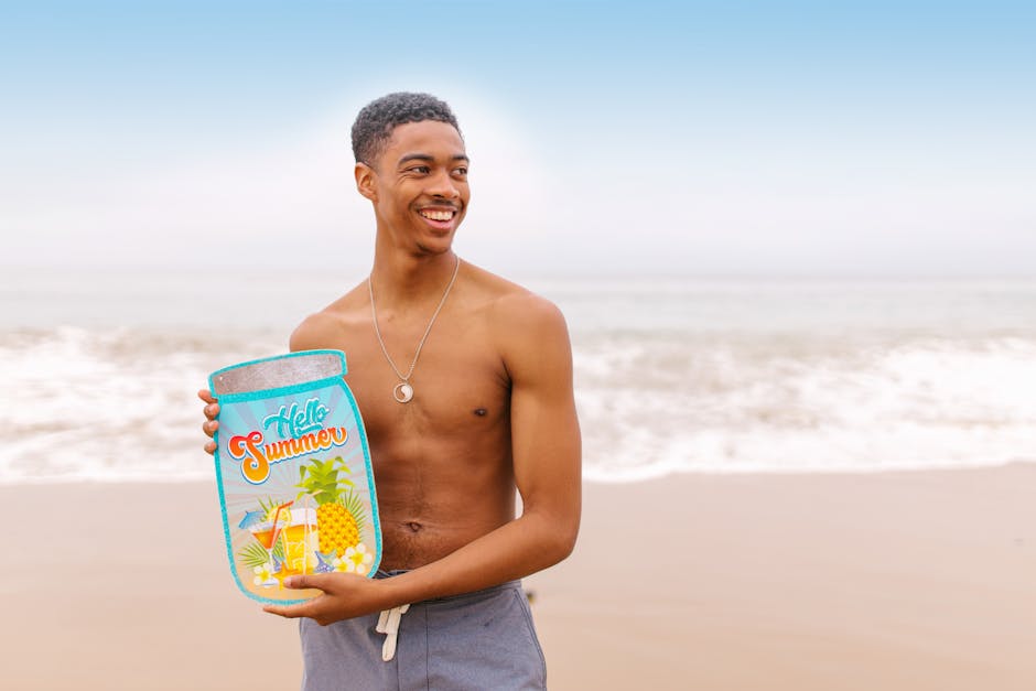 Shirtless man smiling at the beach holding a 'Hello Summer' placard under a bright sky.